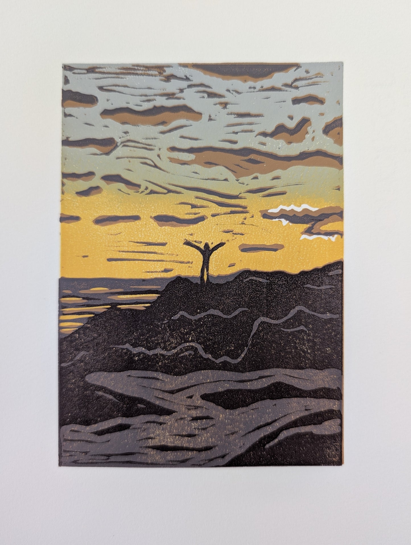 A print featuring a stylized landscape scene with a small figure standing on a dark ridge under a yellow and gray sky, showing the clean paper border.